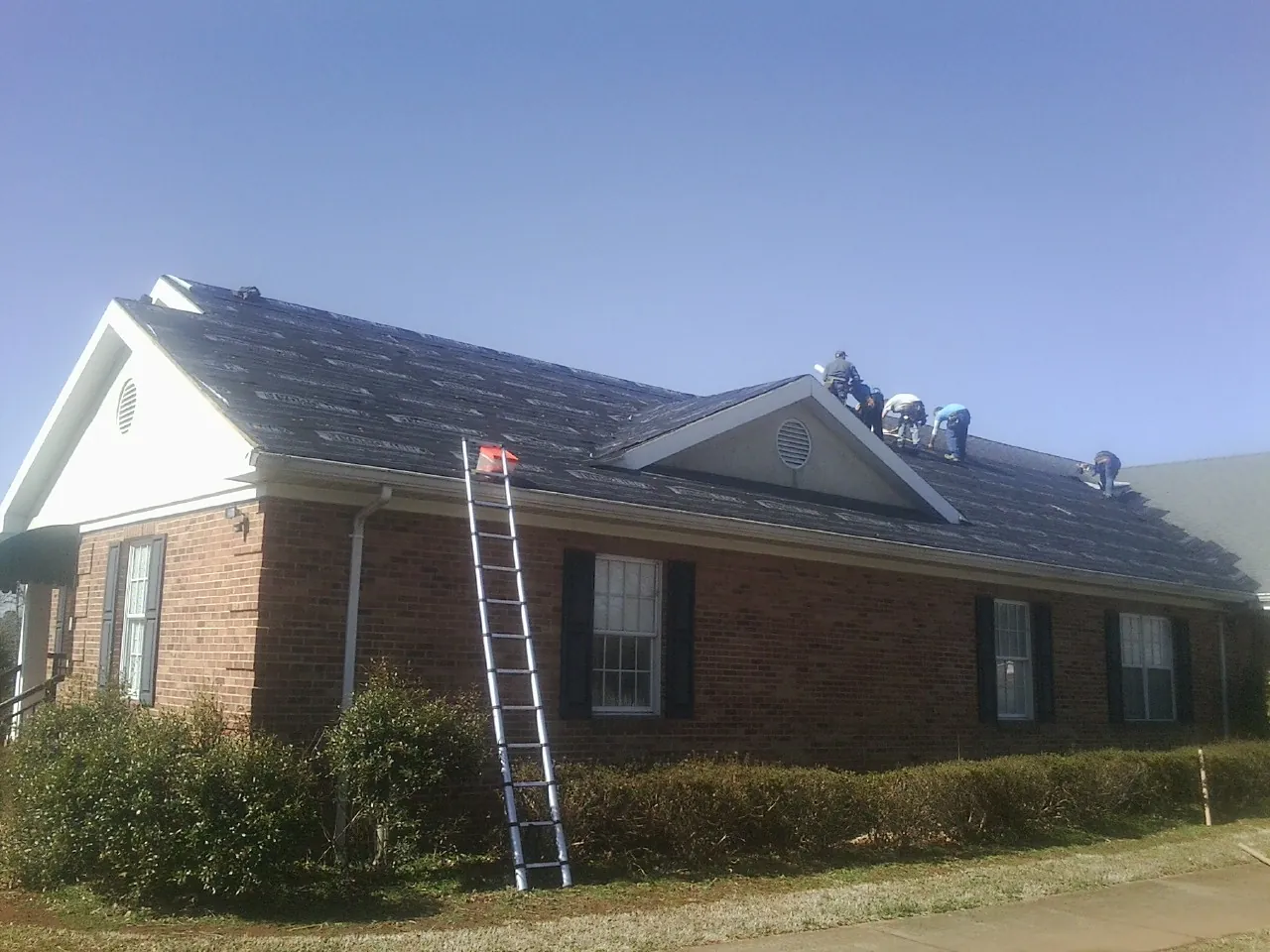 Crew tearing shingles off a brick ranch roof with a ladder set — Metal Roof Repair work by our crew in Hope Valley