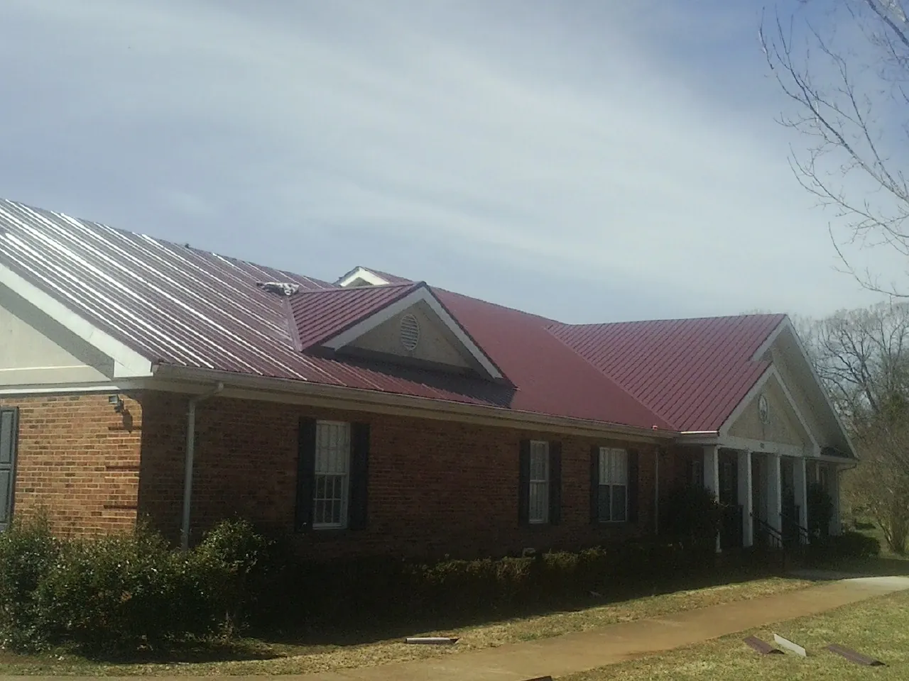 Red metal roof with gabled entries on a long brick building, from a Hail Damage Roof Repair job in Hope Valley