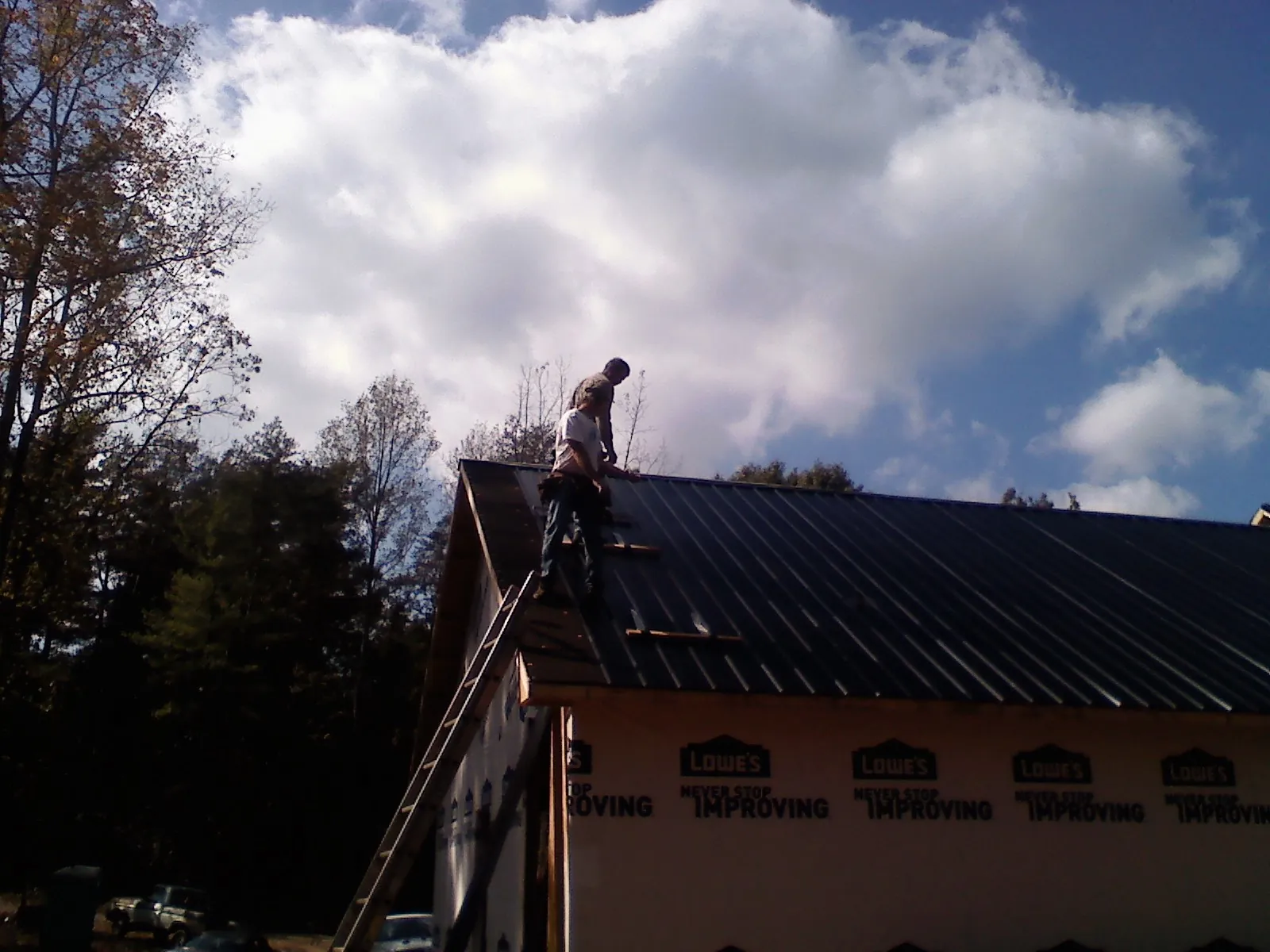 Roofer fastening dark metal panels high against a cloudy sky, from a Roof Inspection job in Hope Valley