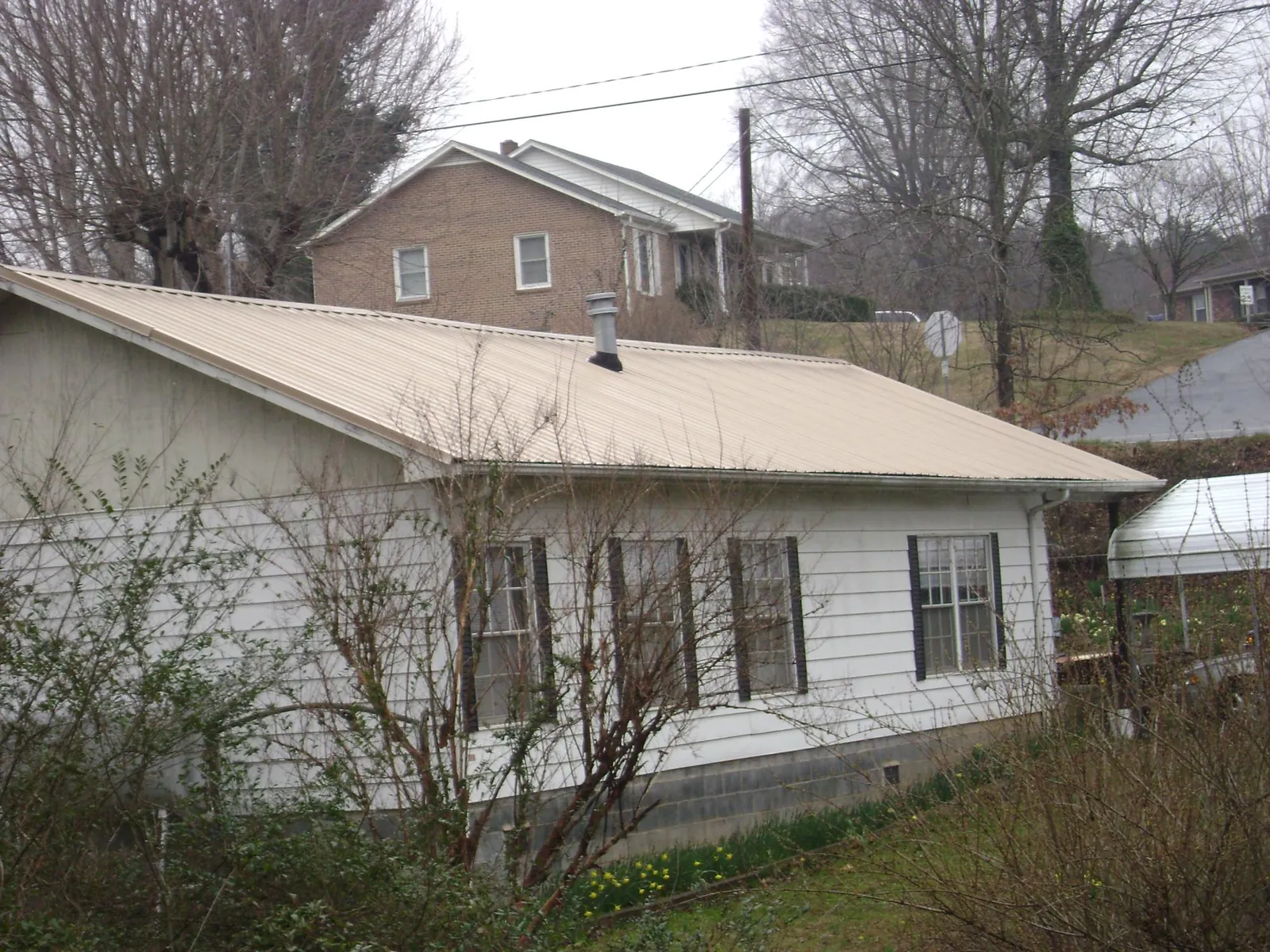 Tan metal roof on a white sided house set into a hillside — Commercial Roofing by Roofing Brothers in Hope Valley